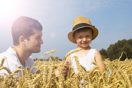 Happy family. Father and son on the wheat field. Male shows the boy ear of wheat.の写真素材