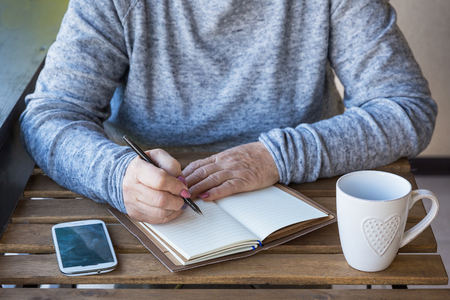 An older woman writes a day plan on a calendar. Next to it is a cup of tea. Business concept. Close up.の写真素材