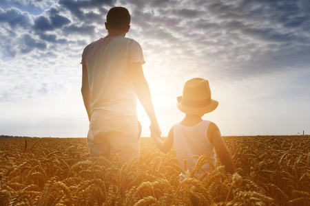 Happy family. Father and son looking at the sun in the wheat field. Backview. の写真素材