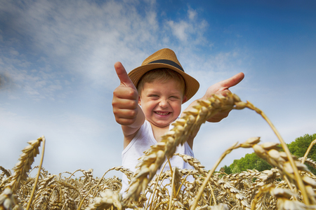 Happy family. Little charming happy boy in a hat laughs in the wheat field. Front view.の写真素材