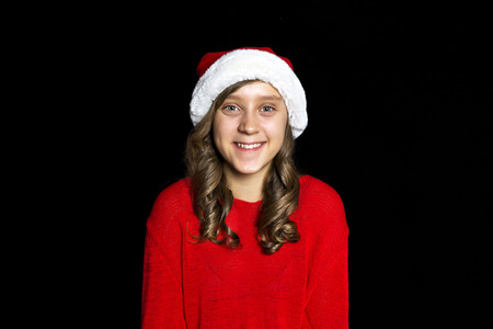 Smiling young girl in red sweater and Santa's hat looks at the viewer. Black isolate. Copy space.の写真素材