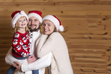 Happy family. Mom, dad and tiny daughter in Santa Claus's hat on a wooden background.の写真素材