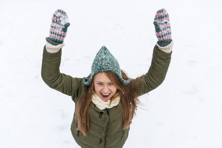 A young beautiful girl with long blond hair enjoys the first snow. Green jacket, green hat and gloves. Top view. Copy space.の写真素材