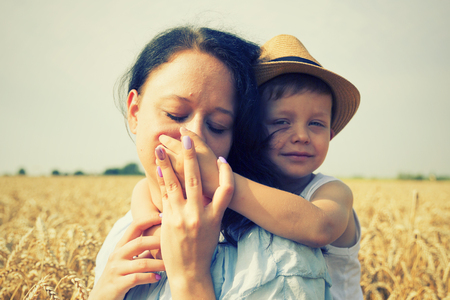 Happy family. Mom and son are laughing and talking on the wheat field. Front view.の写真素材