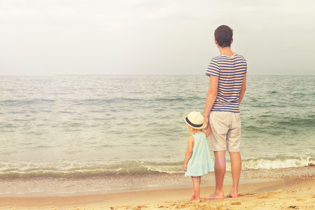 Father and daughter stand on the beach and look at the sea. Back view, copy space.の写真素材