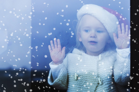 Happy family. Little girl in a cap santy sitting on the window sill at the window, waiting for Christmas.の写真素材