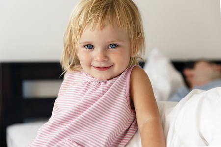 Happy family. A tiny blond girl woke up earlier. Her dad sleep yet. She smiles at the viewer.の写真素材