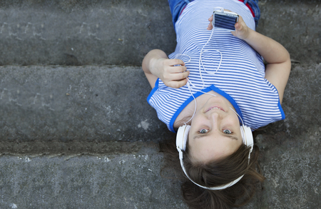Young pretty teenager girl with blond hair listen music in white headset in city park. Copy space.の写真素材