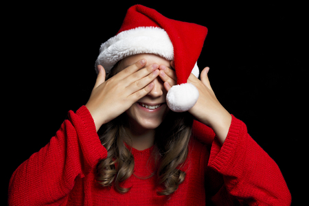 Merry Christmas. Young girl in red sweater and Santa Claus hat closes she's eyes. Black isolate. Copy space.の写真素材