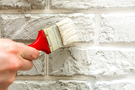 Male's hand painted with brush white brick wall. Renovation work. White background.の写真素材
