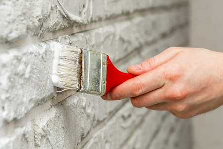 Male's hand painted with brush white brick wall. Renovation work. White background.の写真素材