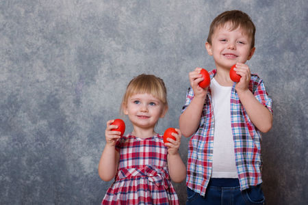 Two children, a girl and a boy dressed in checkered clothes. They hold red wooden Easter eggs in their hands.の写真素材