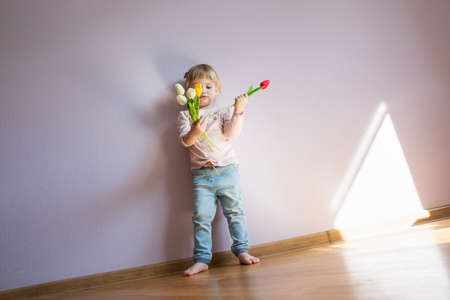 A serious little girl with blond hair is holding a bouquet of colorful tulips in the hands. Shot Full - length. Copy space.の写真素材