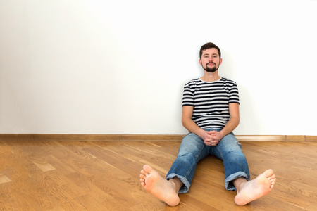 A young man is sitting on the floor in a new apartment. Copy space, white wall.の写真素材