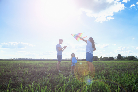 Happy parents and child are flying a kite in the field.の写真素材