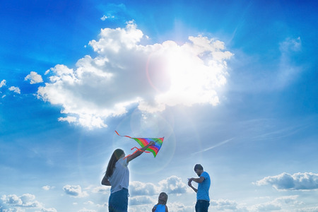 Happy parents and child are flying a kite in the field.の写真素材