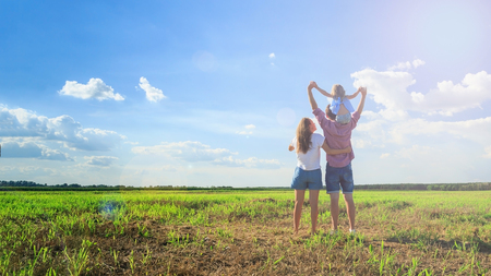 Happy family. Mom dad and daughter look at the sun in the wheat field. Back view.の写真素材