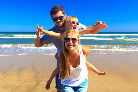 Happy family vacation. Mother father and daughter on the beach. Day light, copy space.の写真素材