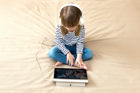 Top wiev portrait of little girl using laptop sitting on the bed.の写真素材
