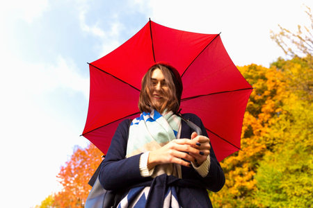 walking woman with red beret and umbrella in sunny autumn parkの写真素材