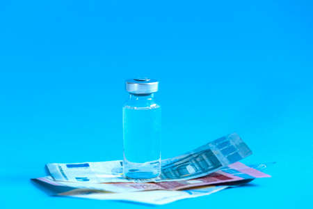 The vaccination cost concept. Glass vial and piggy bank stands on blue background.の写真素材