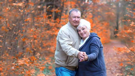 Happy senior couple hugs and looking to camera on an autumn walkの写真素材