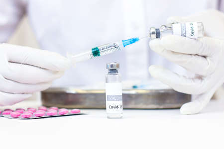 A syringe with a vaccine is held in hands. A vial with a vaccine is on the tableの写真素材