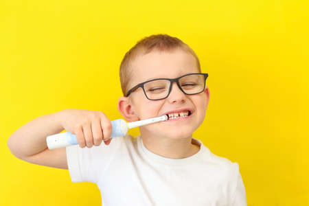 a child in a white T-shirt and glasses is brushing his teethの写真素材
