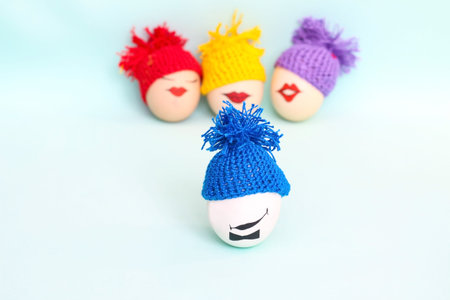 Easter eggs with faces in colorful knitted hats with pompoms