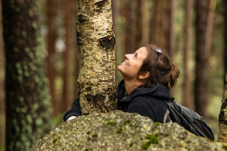 Tourist young woman hugging a tree and smiling in the forest during the mountain hike.Connecting to...