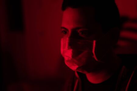 A young man wearing protective mask against the viruses and infections. Concept of protection against viruses and diseases. Red studio lighting. Close up.の写真素材