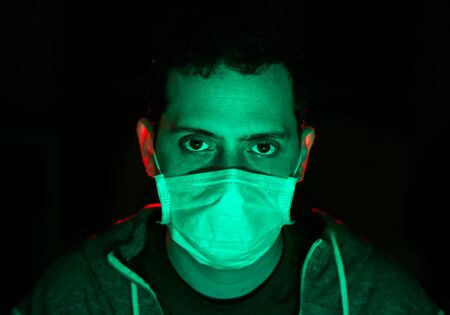 Portrait of a man wearing protective mask against the viruses and infections. Concept of protection against viruses and diseases. Green studio lighting. Close up.の写真素材