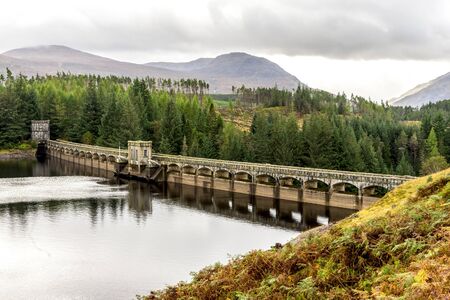 A scenic view of arch curved Laggan Dam with Scottish Highlands in background, Scotlandのeditorial素材