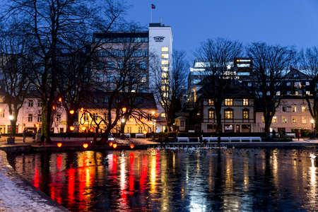 A view to Byparken city park and frozen lake with white swans and decorated trees in winter evening, Stavanger, Norway, December 2017のeditorial素材