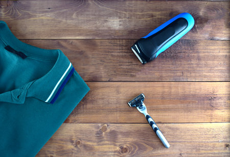 Men flatlyout with polo t-shirt, electrorazor and safety razor on wooden backround. Set of stylish...