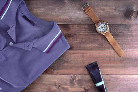 Men flatlyout with polo t-shirt, leather watch and cosmetic tube on wooden backround. Set of stylish man clothes and accessories.の写真素材