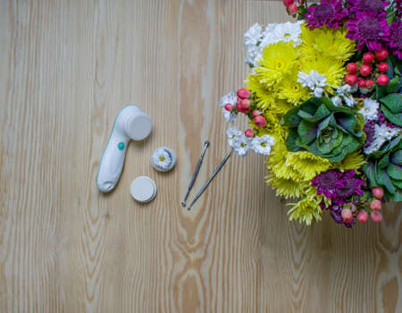 Cosmetic flat lay with electric scrubber, spoon, loop  and bouquet flowers on wooden background.の写真素材