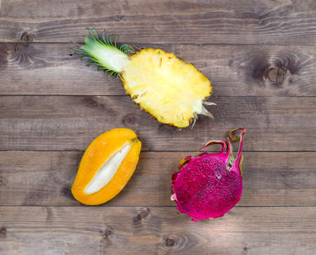 Exotic asia fruits on brown wood background. Assorted tropical summer fruits. Mango, dragon fruit, pitahaya and pineapple. The fresh fruit cut half flat lay.の写真素材