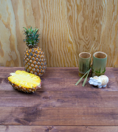 Interior composition of a home on brown wooden table and yellow wall. Handmade spa white elephant candle. Tropical fruit fresh pineapple and cut half. Decorative bamboo glasses from Thailand. の写真素材