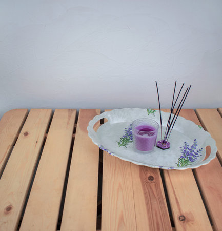 Oval tray with aroma sticks and candle lavender in a glass on light wood table. Spa flat lay.