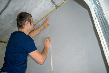 Home redecoration, young man glues wallpaper. Wallpapering in apartment.