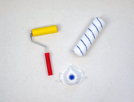 Paint roller with red handle, yellow smooth and soft velour nozzles with medical mask isolated. Industrial respirator with valve protects against dust. Tool, roller for smoothing wallpaper.の写真素材