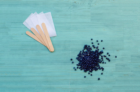 Flat lay beauty cosmetology tools for depilation body. Wax granules lavender with wood spatulas and...