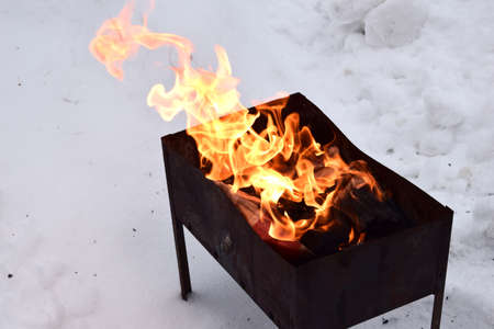 Coals burning wood and bokeh fire ash blaze mangal barbeque. Small mangal with flame in forest. Campfire in winter.の写真素材