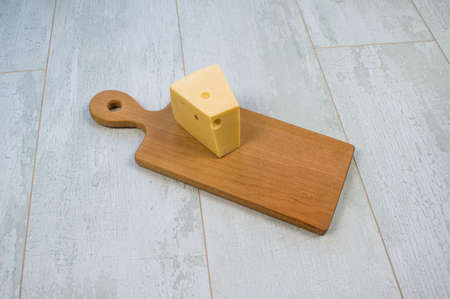 Aged italian fresh cheddar cheese served on wooden cutting plate isolated over wooden background.の写真素材
