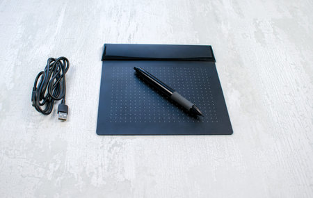 Black graphic digital tablet with pen for illustrators and designers, isolated on a light wood...