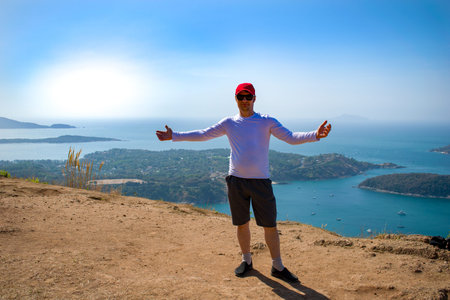 The young man shows his hand at the view from the mountain. Sportswear, cap. The Andamand Sea of...