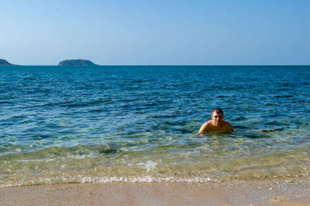 A happy young man swim in the sea. Beautiful landscape of exotic white sand sea beach and palm trees Southeast Asia, Thailand.の写真素材