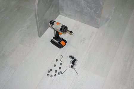 Tools to assemble furniture on the wooden floor. Wireless electric screwdriver, bolts.
