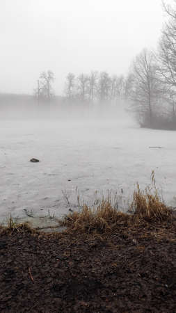 Autumn or spring season. Gloomy landscape. Thick fog over the ice lake.の写真素材